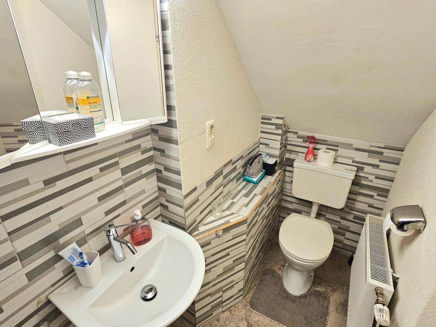 Kompaktes WC mit Toilette, Waschbecken und schrägen Wänden unter dem Dach.