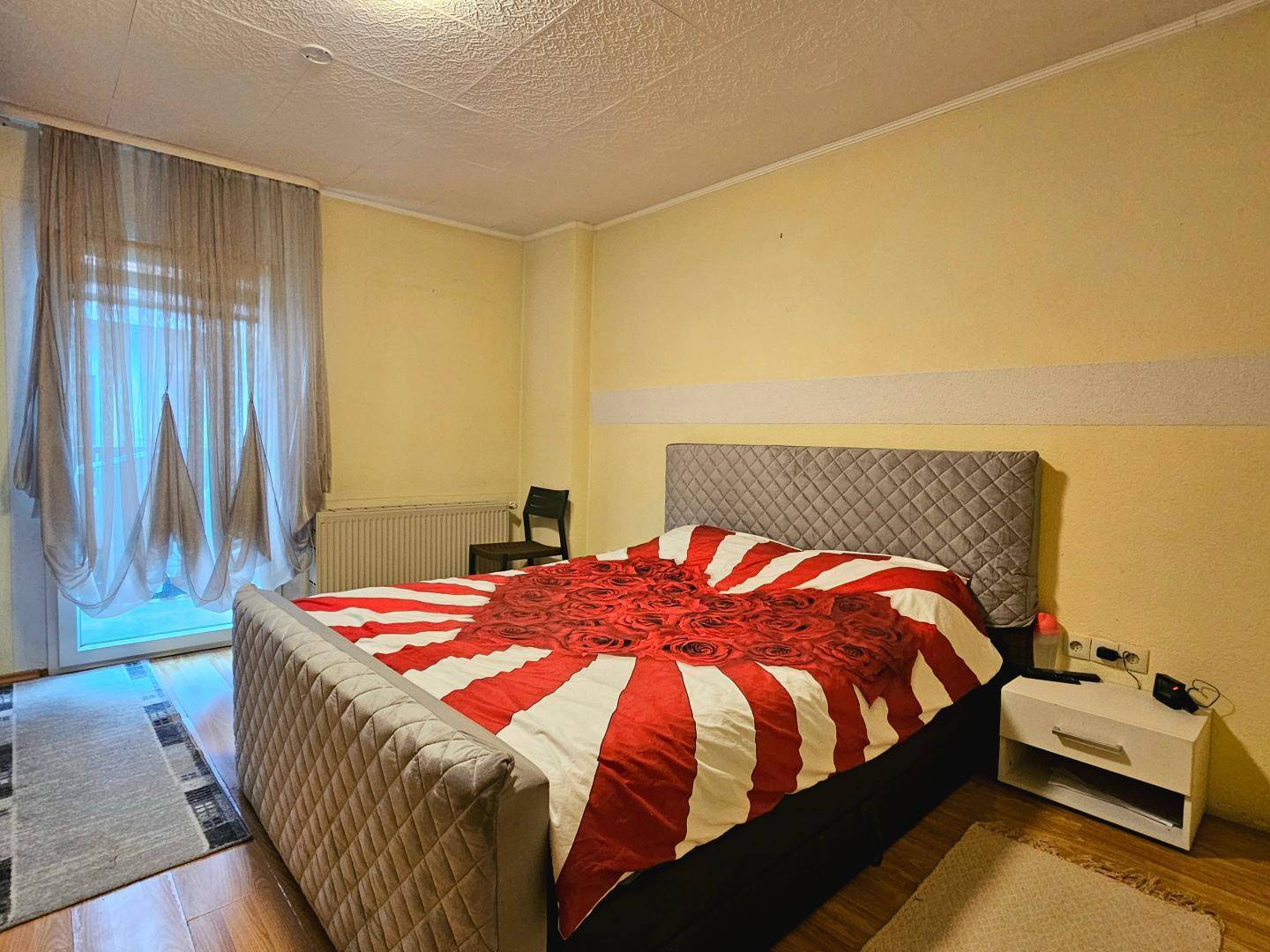 Helles Schlafzimmer mit Doppelbett, farbiger Bettwäsche und Zugang zu einem Balkon.