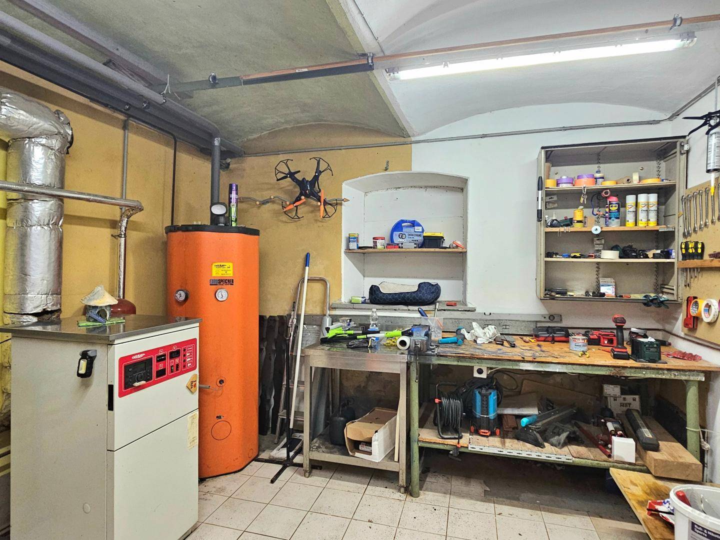 Geräumiger Werkstatt- und Heizungsraum mit Boiler, Werkbank und Lagerregalen.