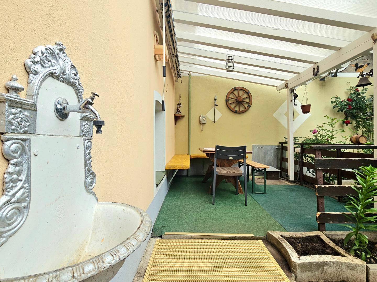 Überdachte Terrasse mit Sitzgelegenheiten, dekorativem Brunnen und Pflanzen für Entspannung.