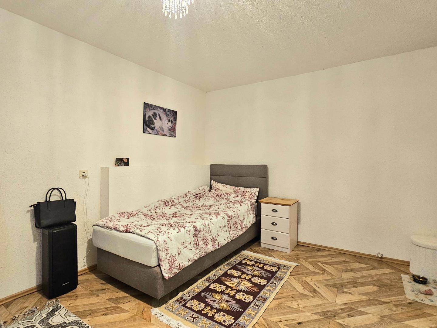 Kleines Schlafzimmer mit Einzelbett, Teppich und schlichten Möbeln.