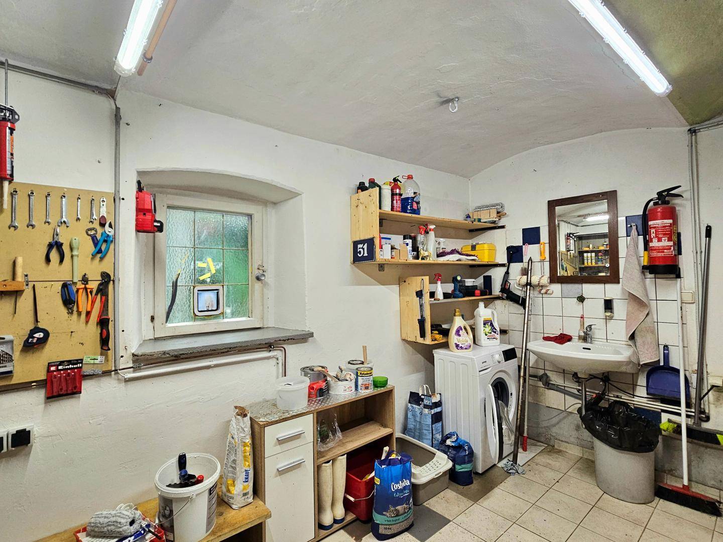 Funktionaler Kellerraum mit Waschmaschine, Spülbecken und Werkzeugen an der Wand.