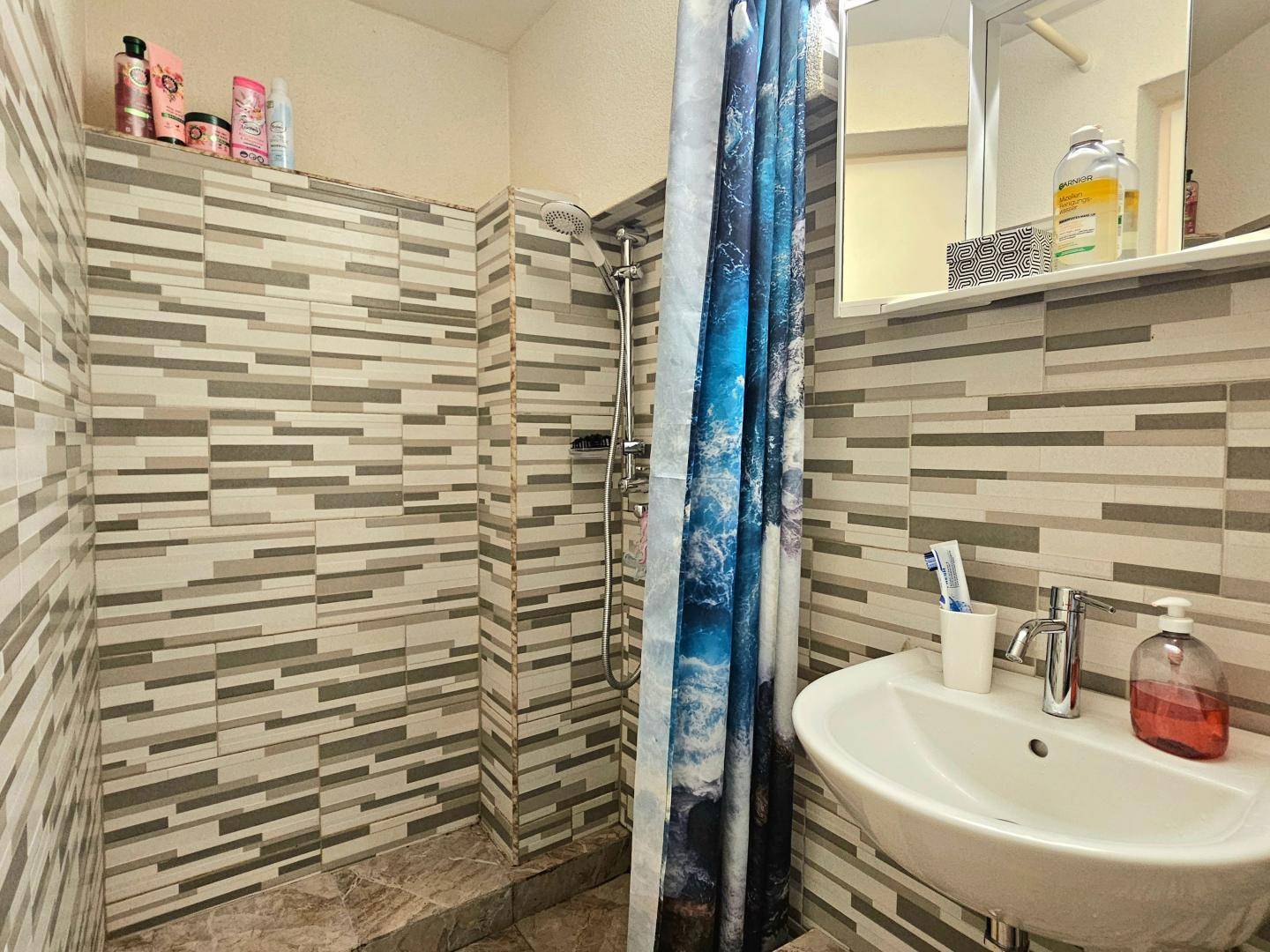 Modern gefliestes Badezimmer mit Dusche und Waschbecken in minimalistischem Design.