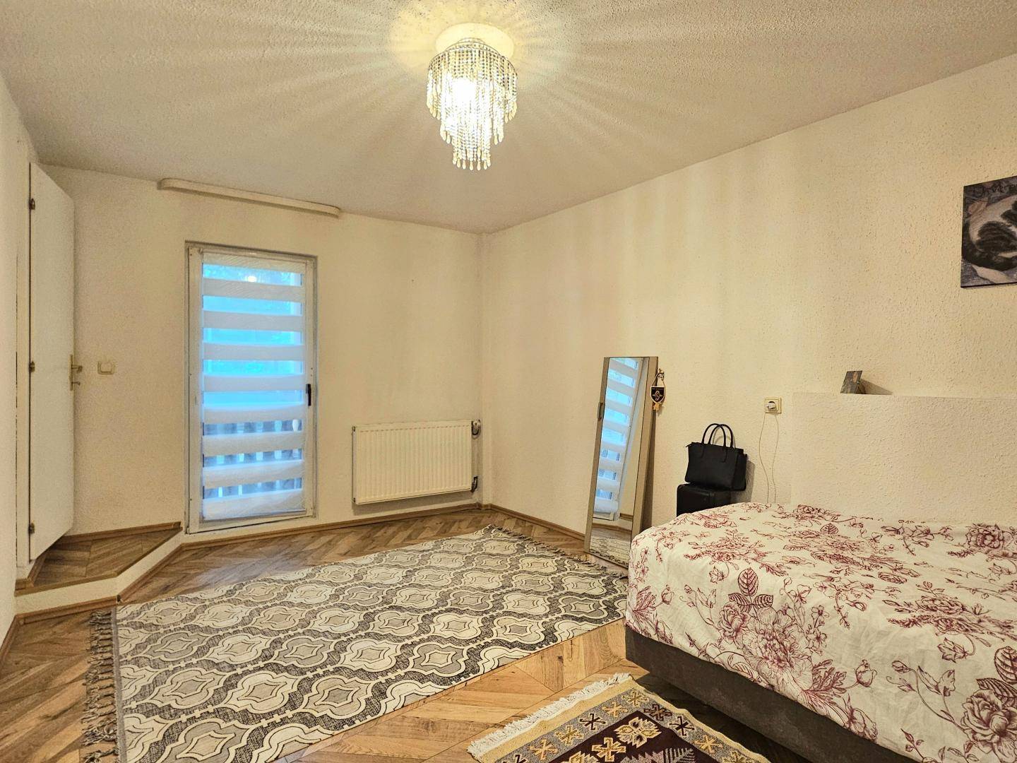 Schlafzimmer mit Einzelbett, Teppich und Zugang zu einem Außenbereich durch eine Tür.
