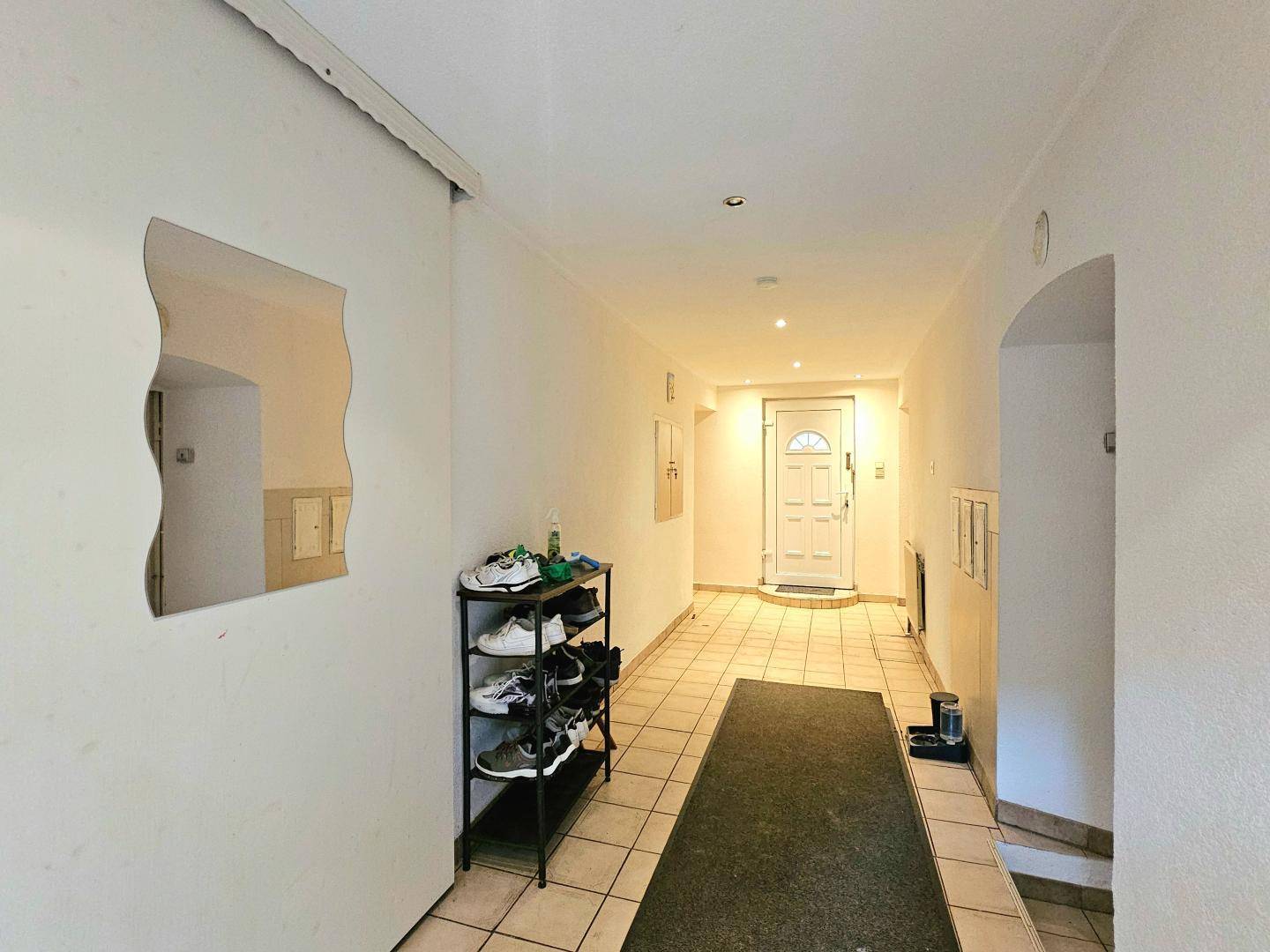 Heller Eingangsbereich mit Fliesenboden, Schuhregal und weißer Eingangstür.