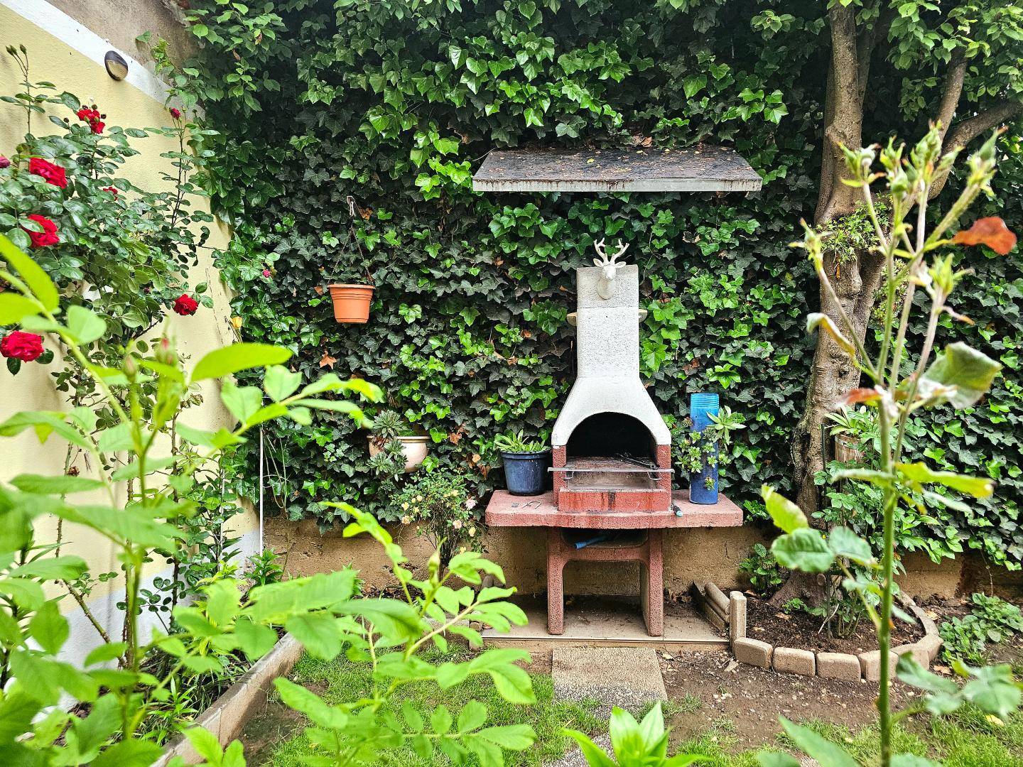 Gemütlicher Gartenbereich mit festem Grillplatz, umgeben von üppigem Grün und Efeu.