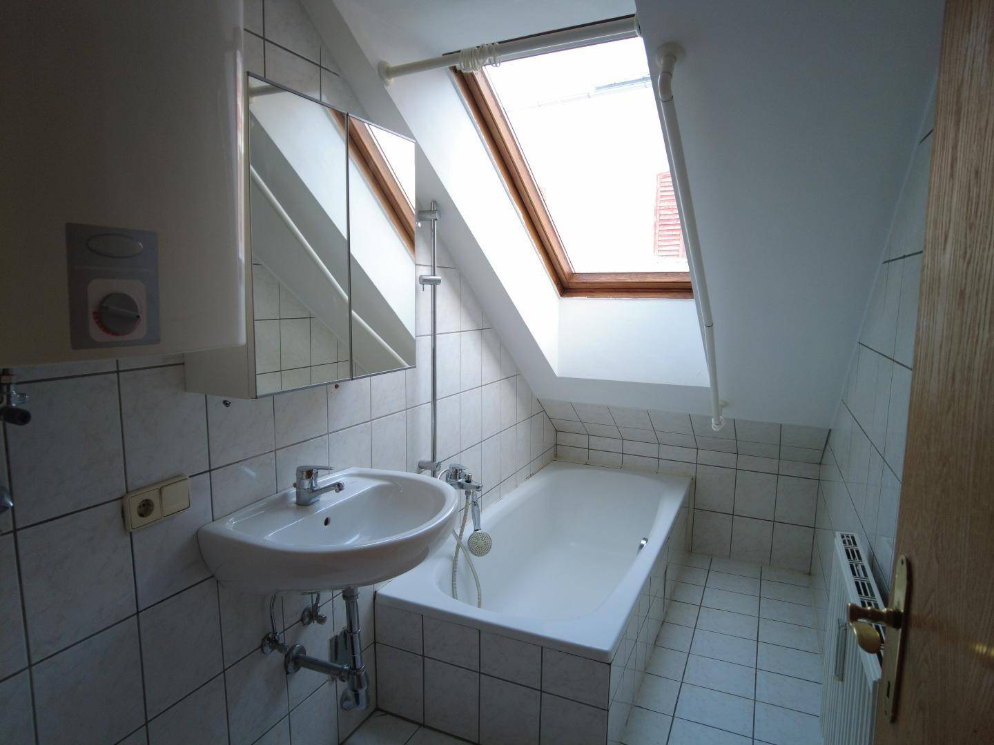 Gefliestes Badezimmer im Dachgeschoss mit Badewanne, Waschbecken und Dachfenster.