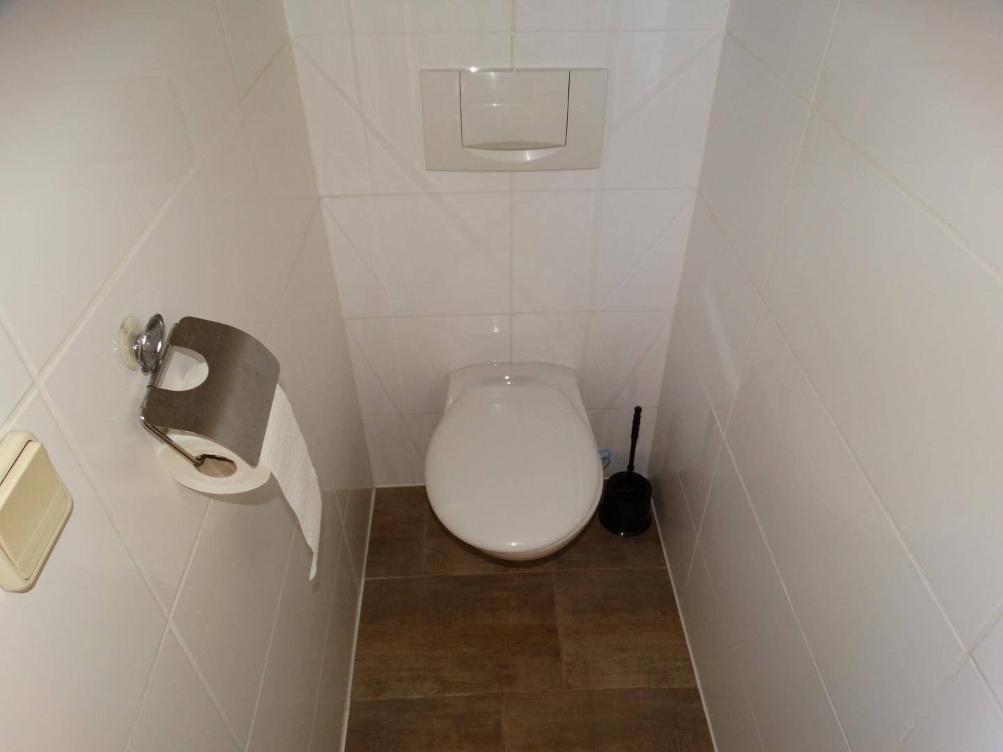 Kleines, gefliestes Gäste-WC mit wandhängender Toilette und Spülkasten.