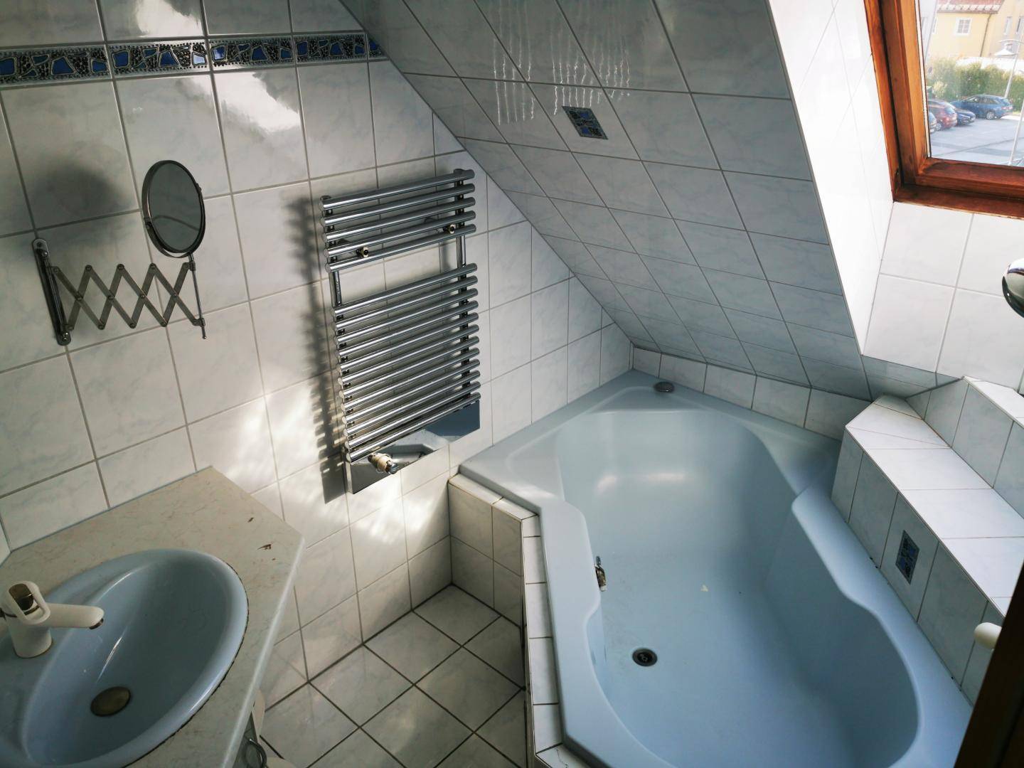 Gefliestes Badezimmer im Dachgeschoss mit Eckbadewanne, Waschbecken und beheiztem Handtuchhalter.