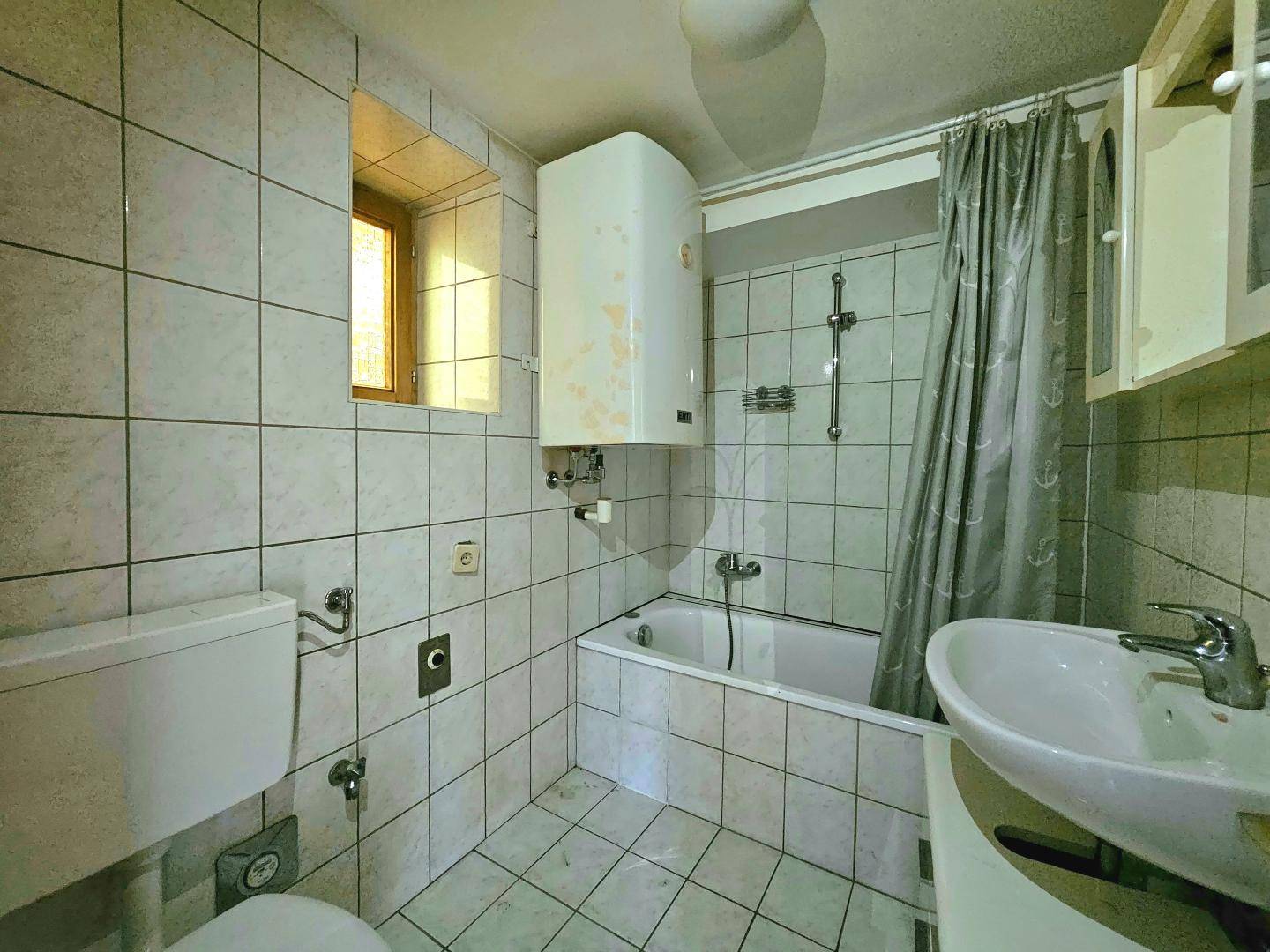 Gefliestes Badezimmer mit Badewanne, Waschbecken und Toilette, ausgestattet mit einem Boiler.