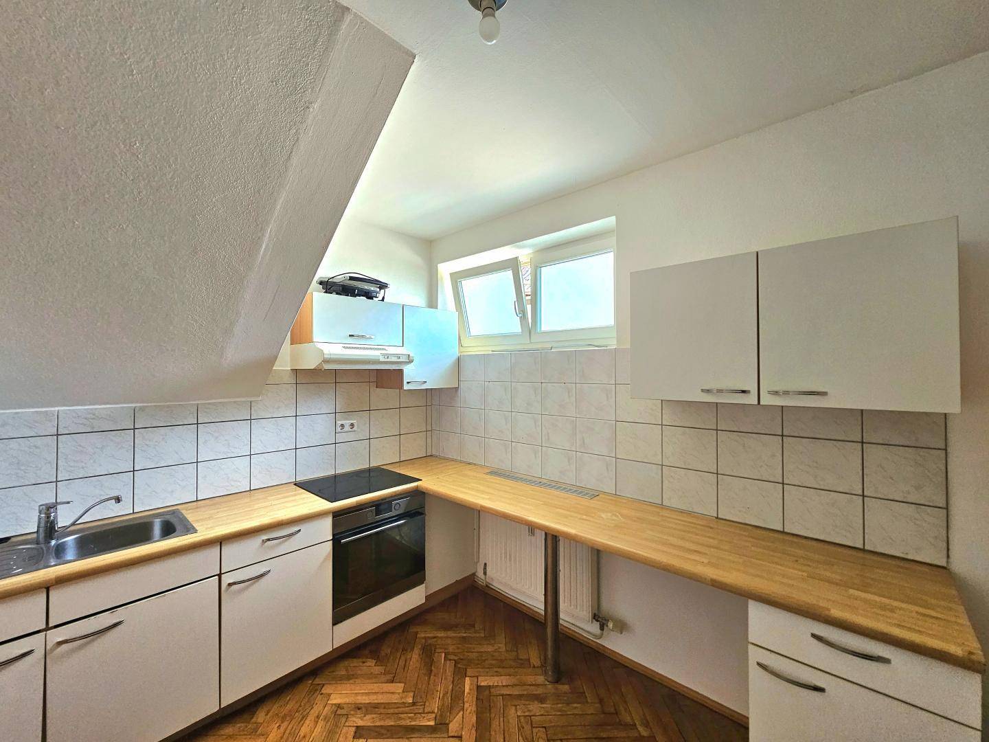 Funktionale Küche mit weißen Schränken, Holzarbeitsplatte und Dachschräge.
