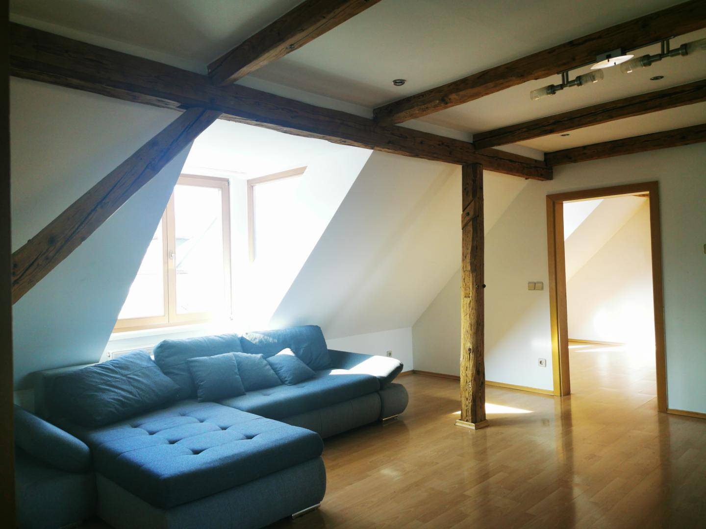 Gemütliches Wohnzimmer im Dachgeschoss mit sichtbaren Holzbalken und viel Tageslicht.