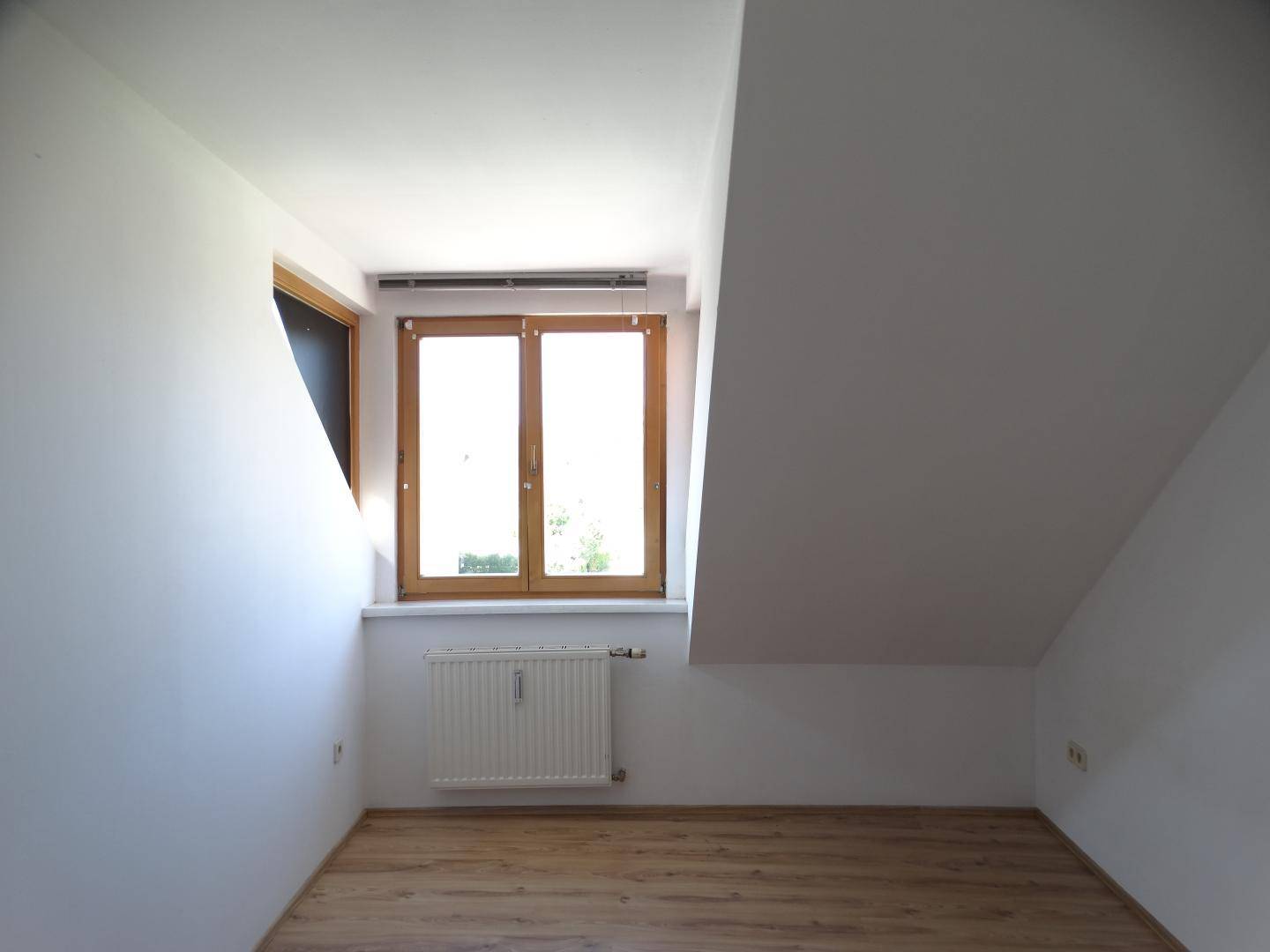 Helles Zimmer im Dachgeschoss mit Holzboden und Fenster, das viel Tageslicht hereinlässt.