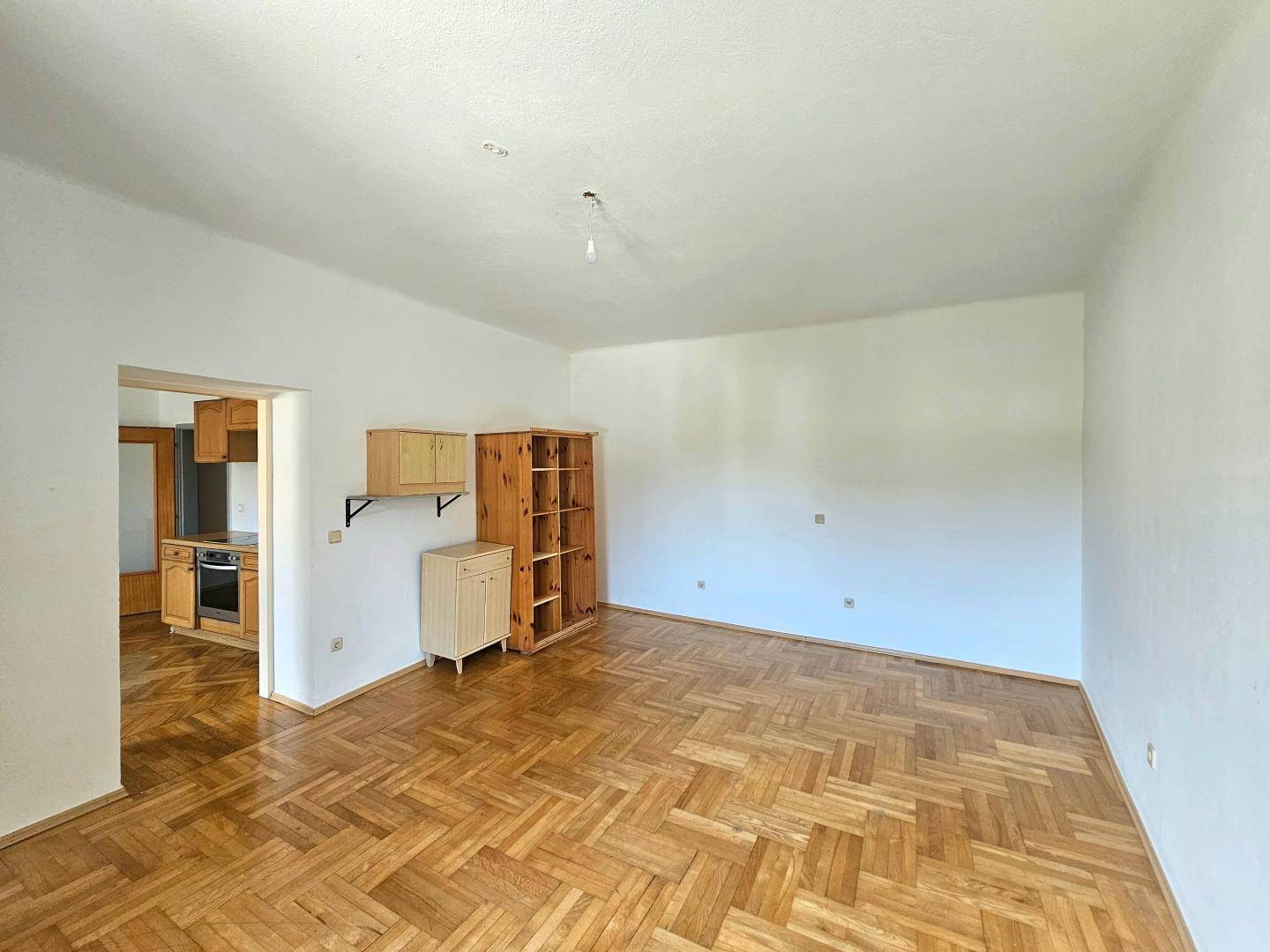 Helles Wohnzimmer mit Fischgrätparkettboden und Zugang zu einer Küche.