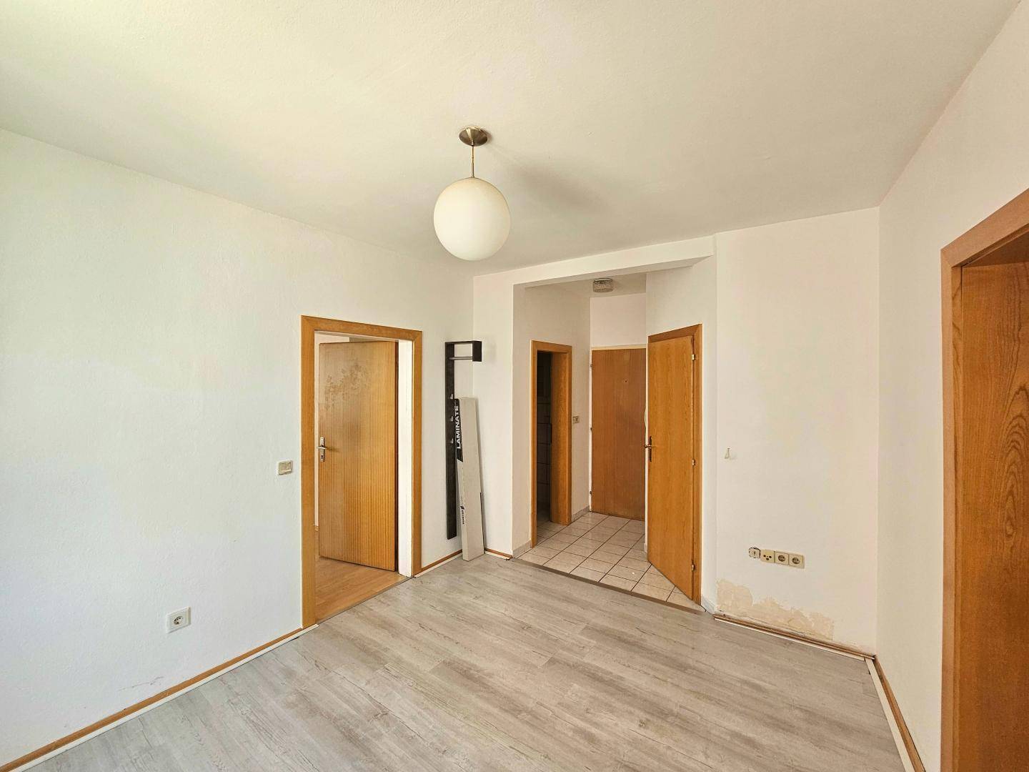 Heller Flur mit Laminatboden, der zu weiteren Räumen mit unterschiedlichen Bodenbelägen führt.