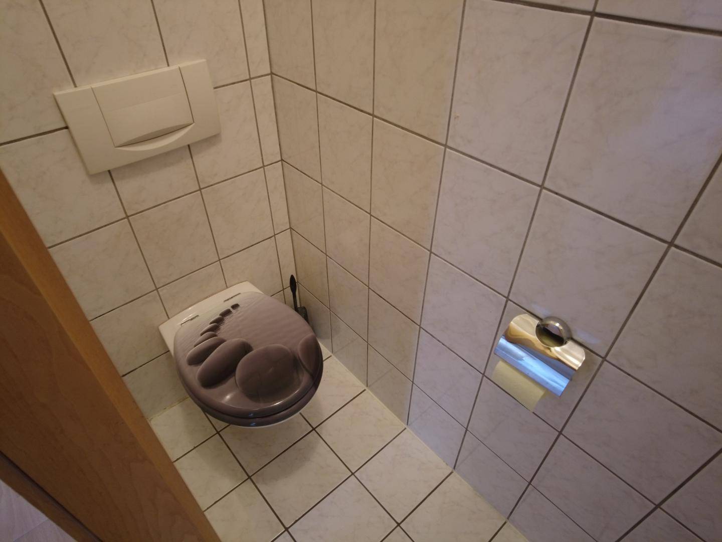 Kleines, gefliestes Gäste-WC mit Toilette und hellem Fliesenboden.