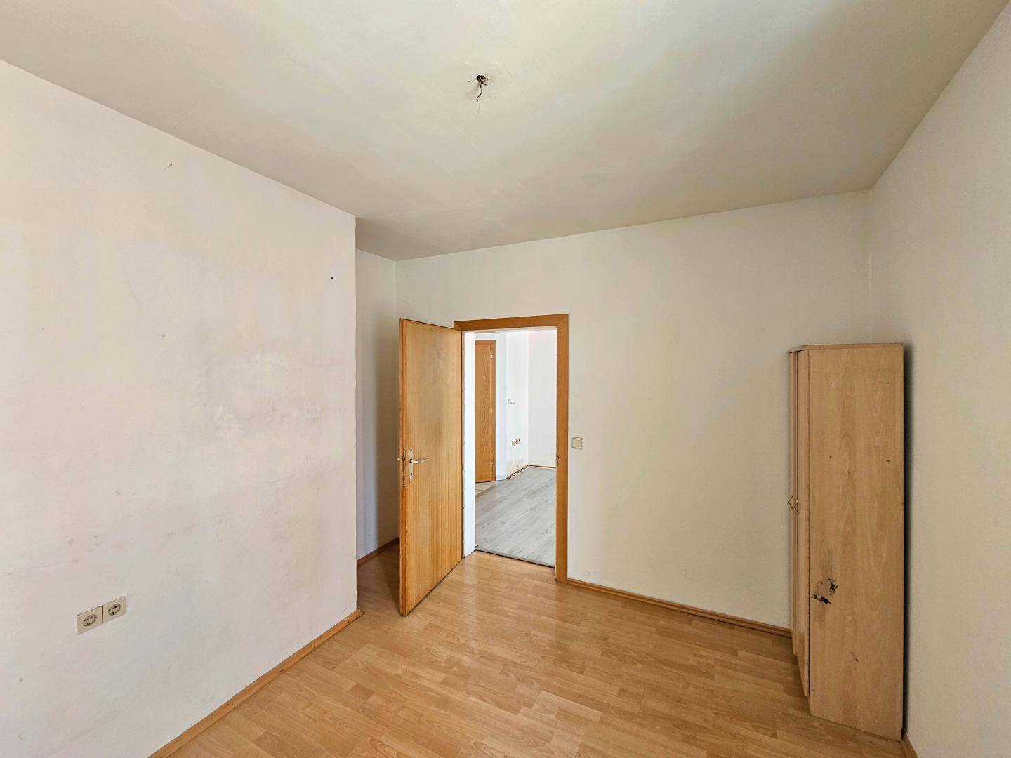 Leeres Zimmer mit hellem Parkettboden und Holztür, bereit zur individuellen Gestaltung.