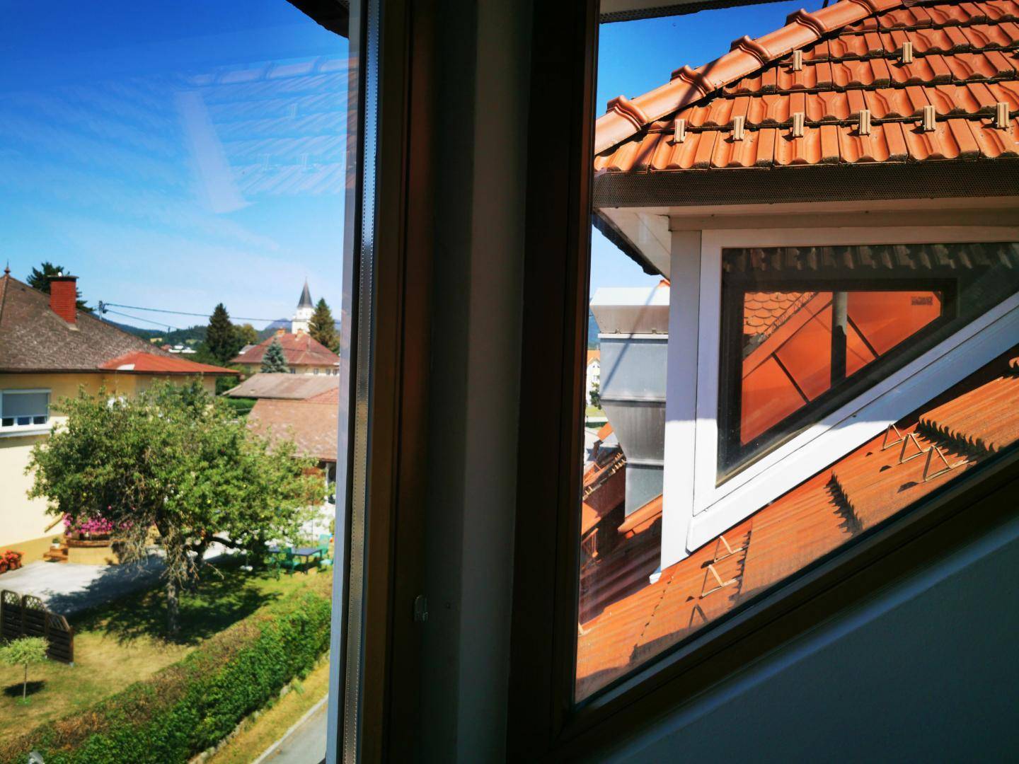 Ausblick aus einem Fenster auf die umliegenden Dächer und die grüne Landschaft.