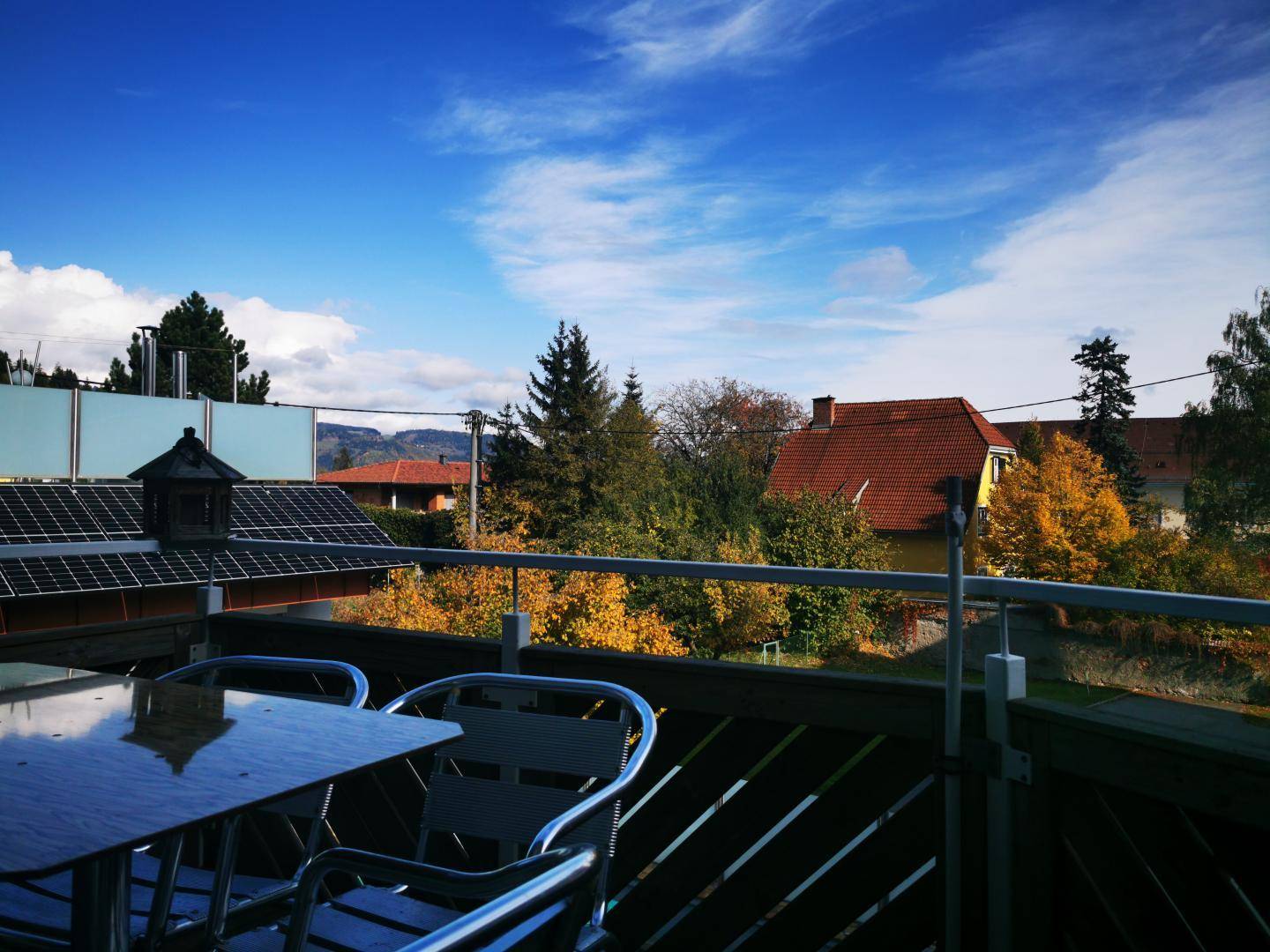 Sonniger Balkon mit Sitzgelegenheiten und Blick auf die umliegende Landschaft und Dächer.