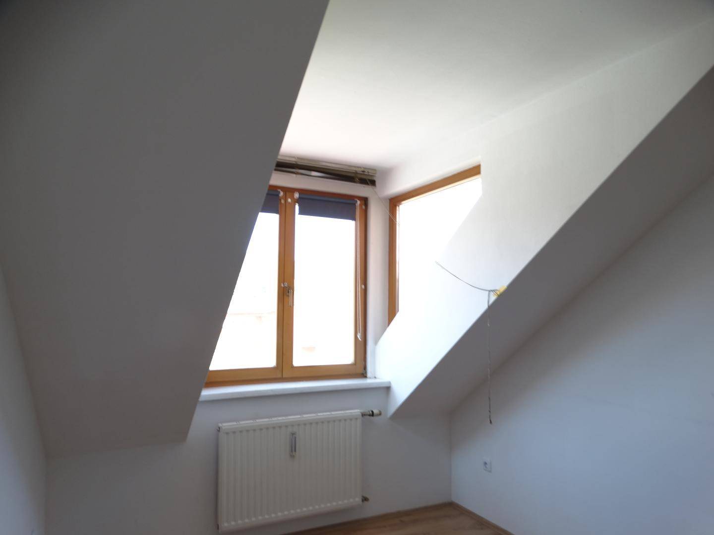 Helles Zimmer im Dachgeschoss mit Holzboden und Fenster, das viel Tageslicht hereinlässt.