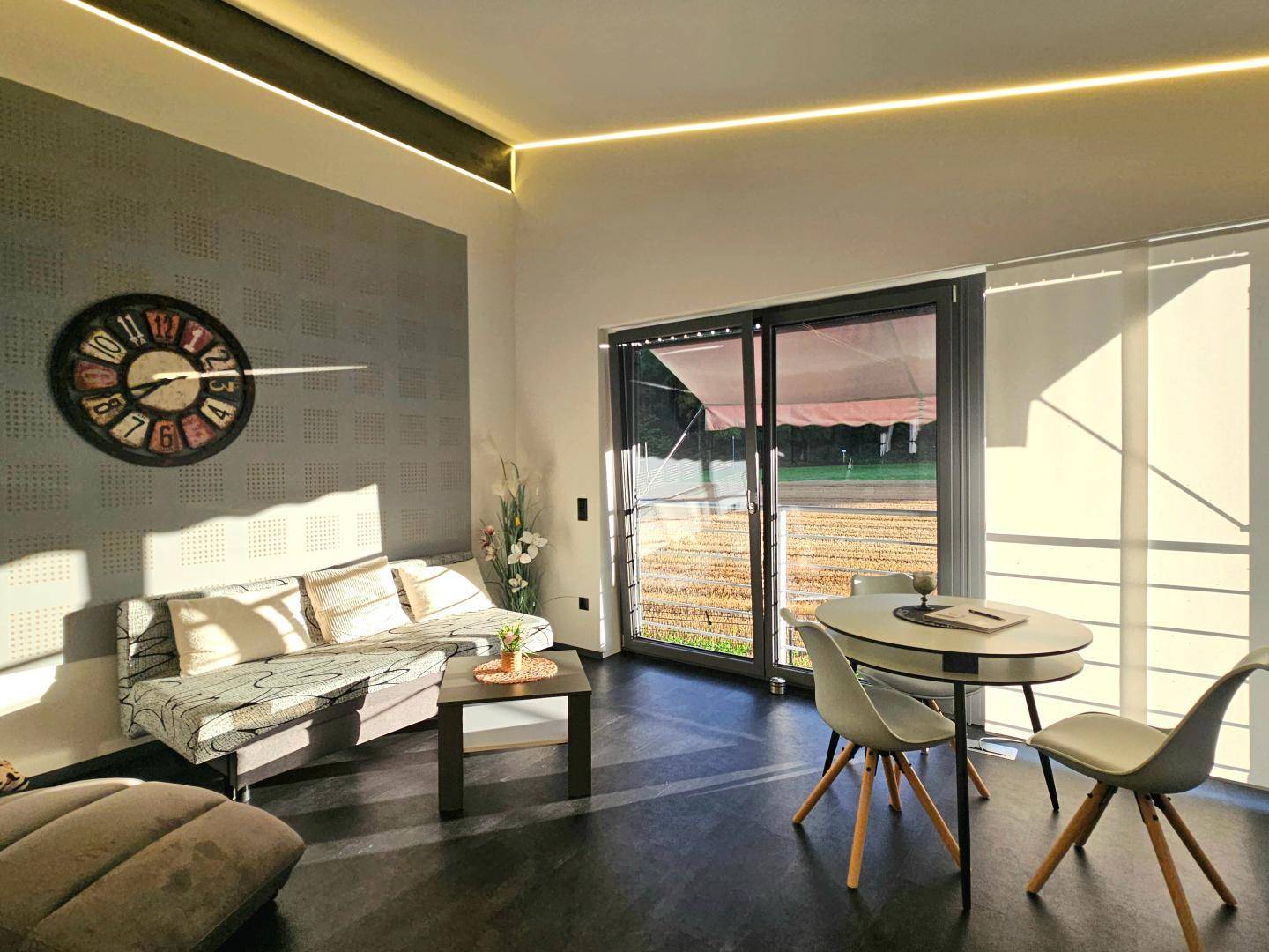 Helles Wohnzimmer mit gemütlicher Sitzecke, Esstisch und indirekter Deckenbeleuchtung.
