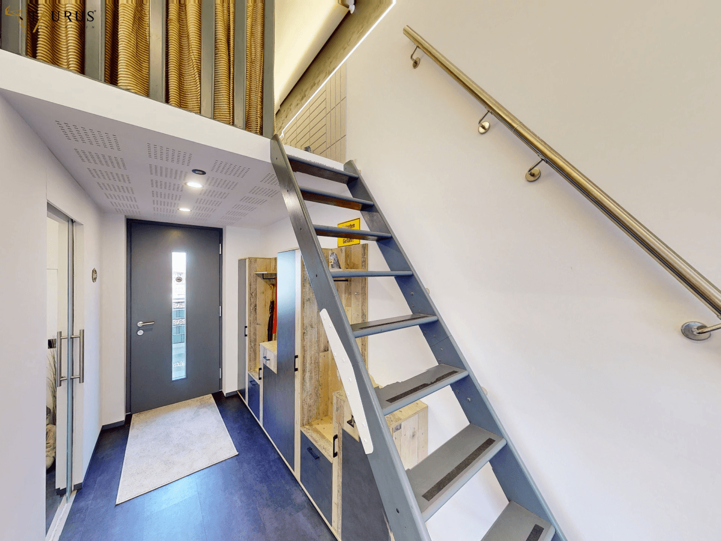 Eingangsbereich mit Garderobe, dunklem Boden und Treppe zu einem erhöhten Schlafbereich.