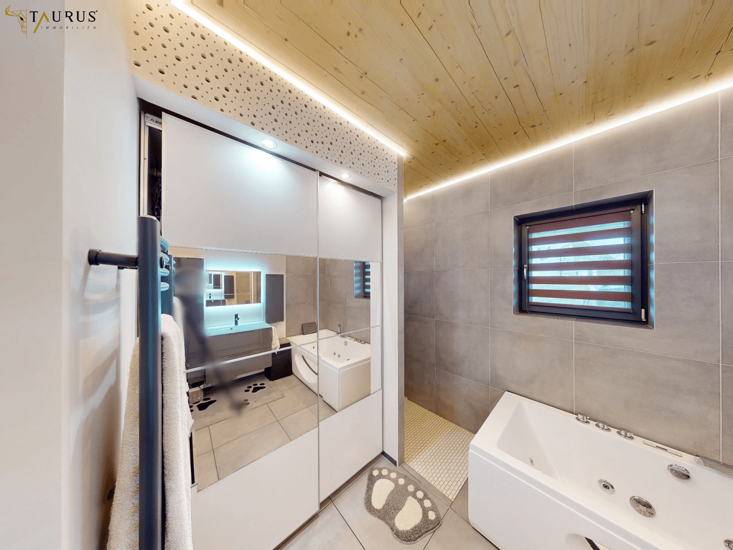 Modernes Badezimmer mit Whirlpool-Badewanne, Spiegelschrank und grauen Fliesen.