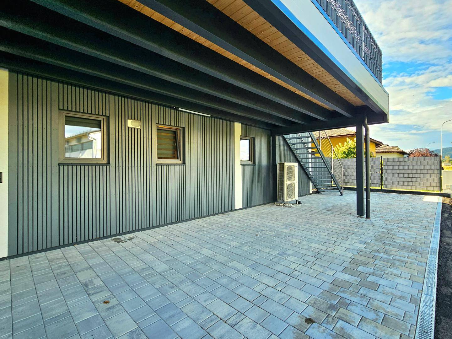 Moderne Gebäudefassade mit Holzverkleidung und gepflastertem Außenbereich.