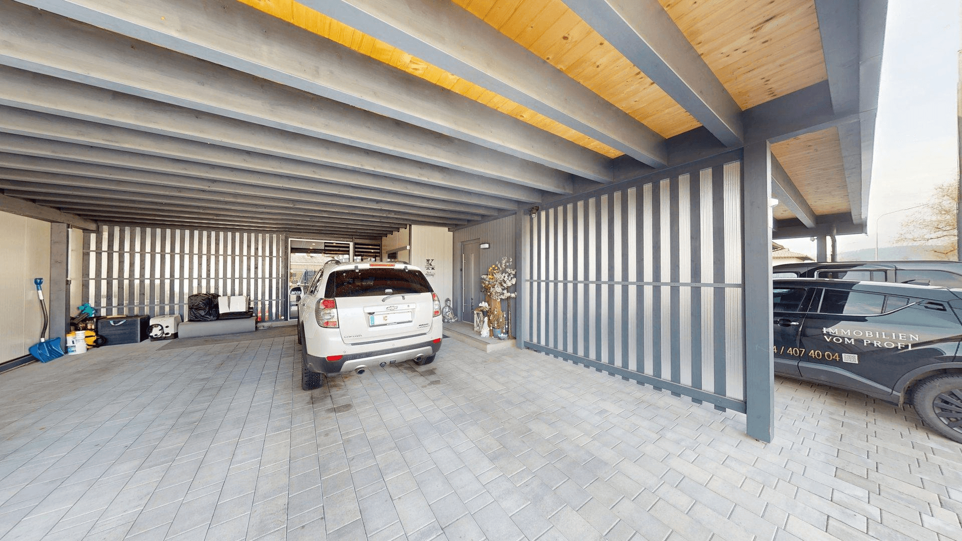 Überdachter Carport mit mehreren Stellplätzen und Holzbalkendecke.