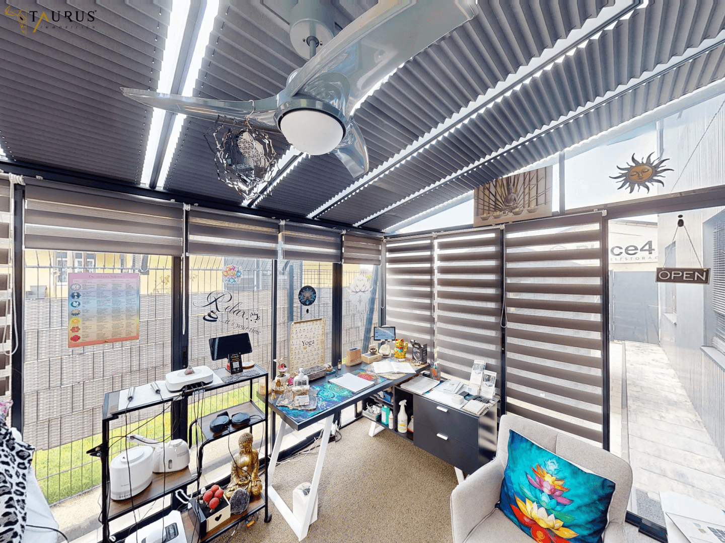 Vielseitiger Wintergarten, als Büro genutzt, mit großen Fenstern und Deckenventilator.