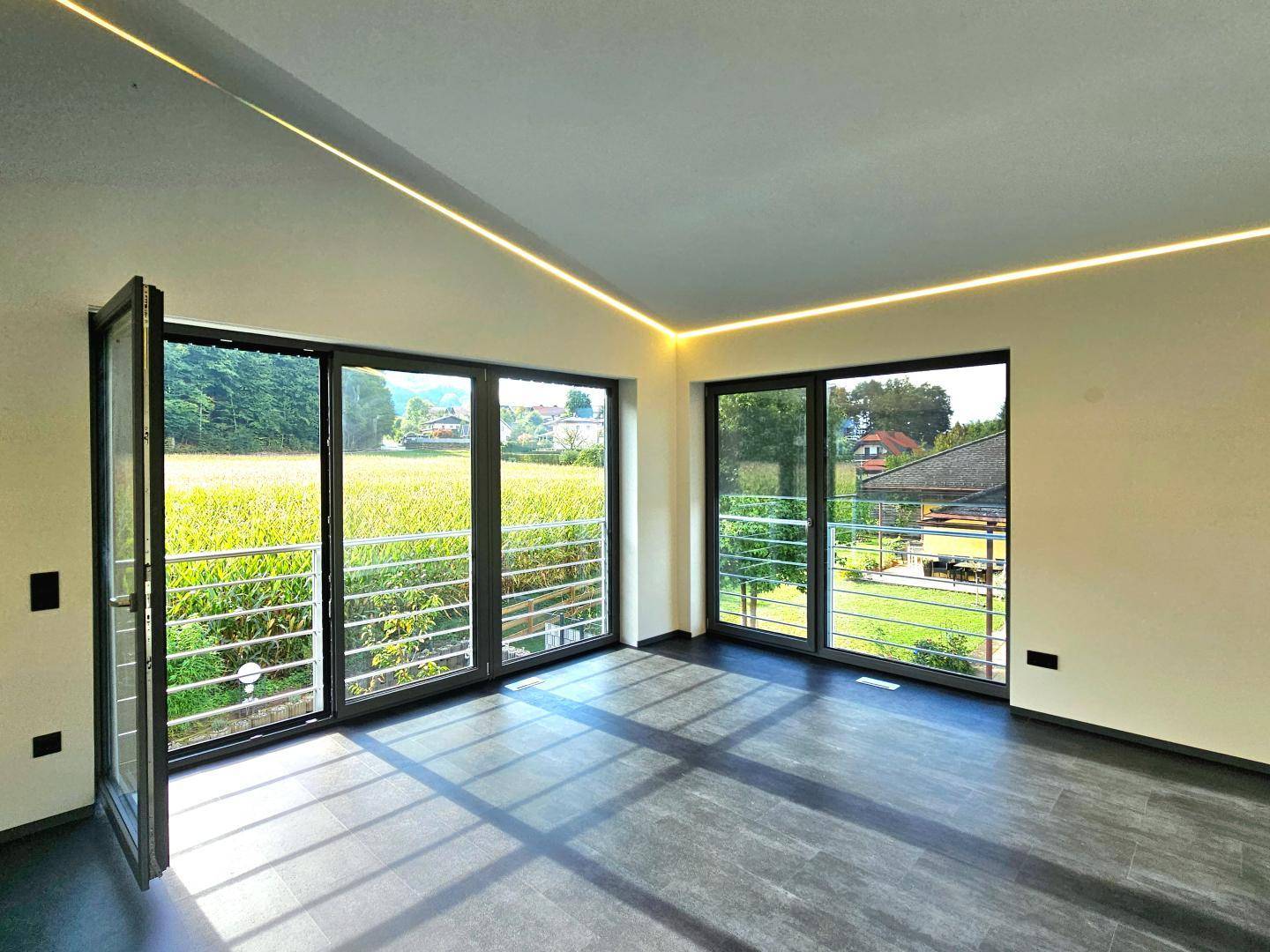 Lichtdurchfluteter Wohnraum mit großen Fensterfronten und Blick ins Grüne.