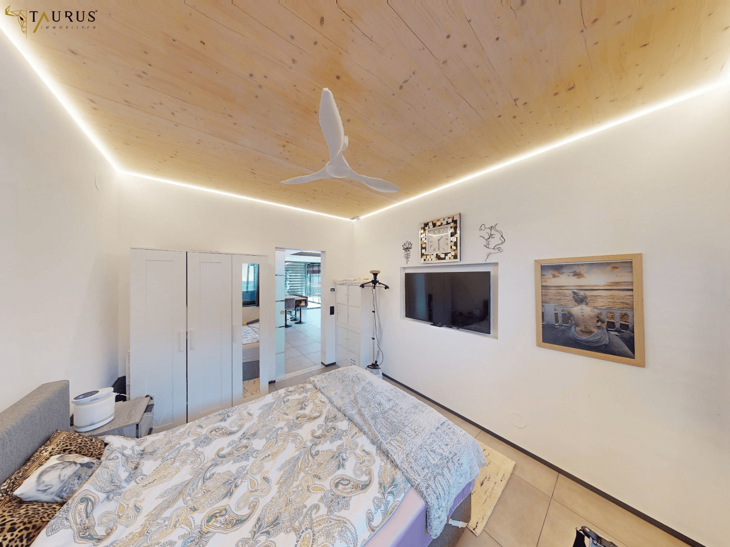 Helles Schlafzimmer mit Holzbalkendecke, Deckenventilator und modernem Bett.