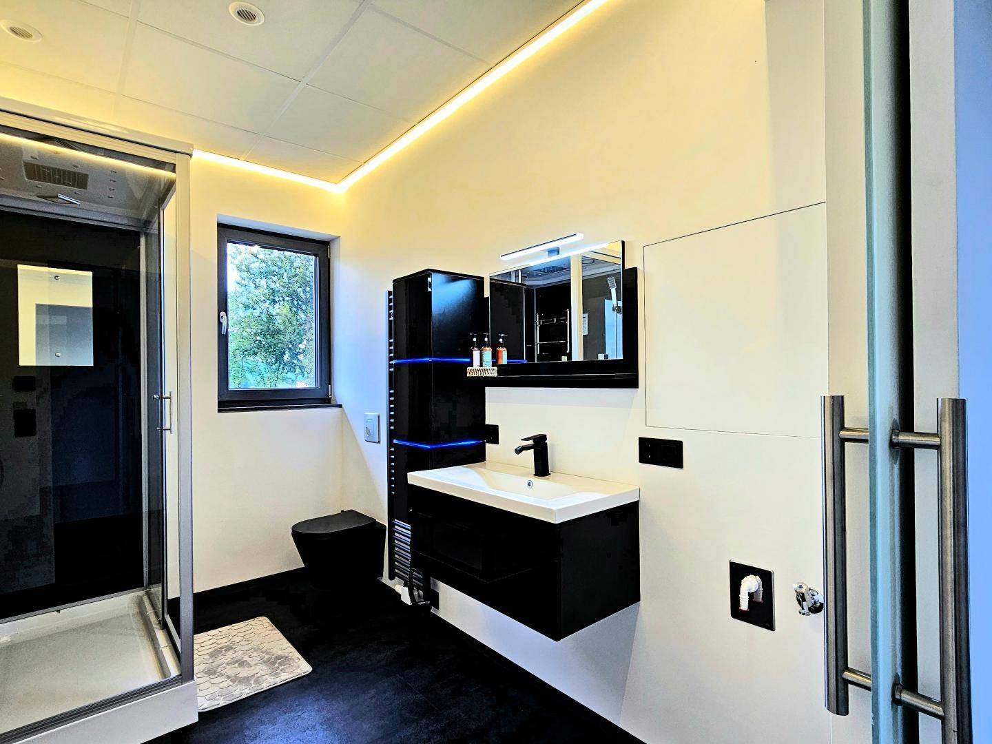 Modernes Badezimmer mit schwarzem Waschtisch, Duschkabine und Fenster.