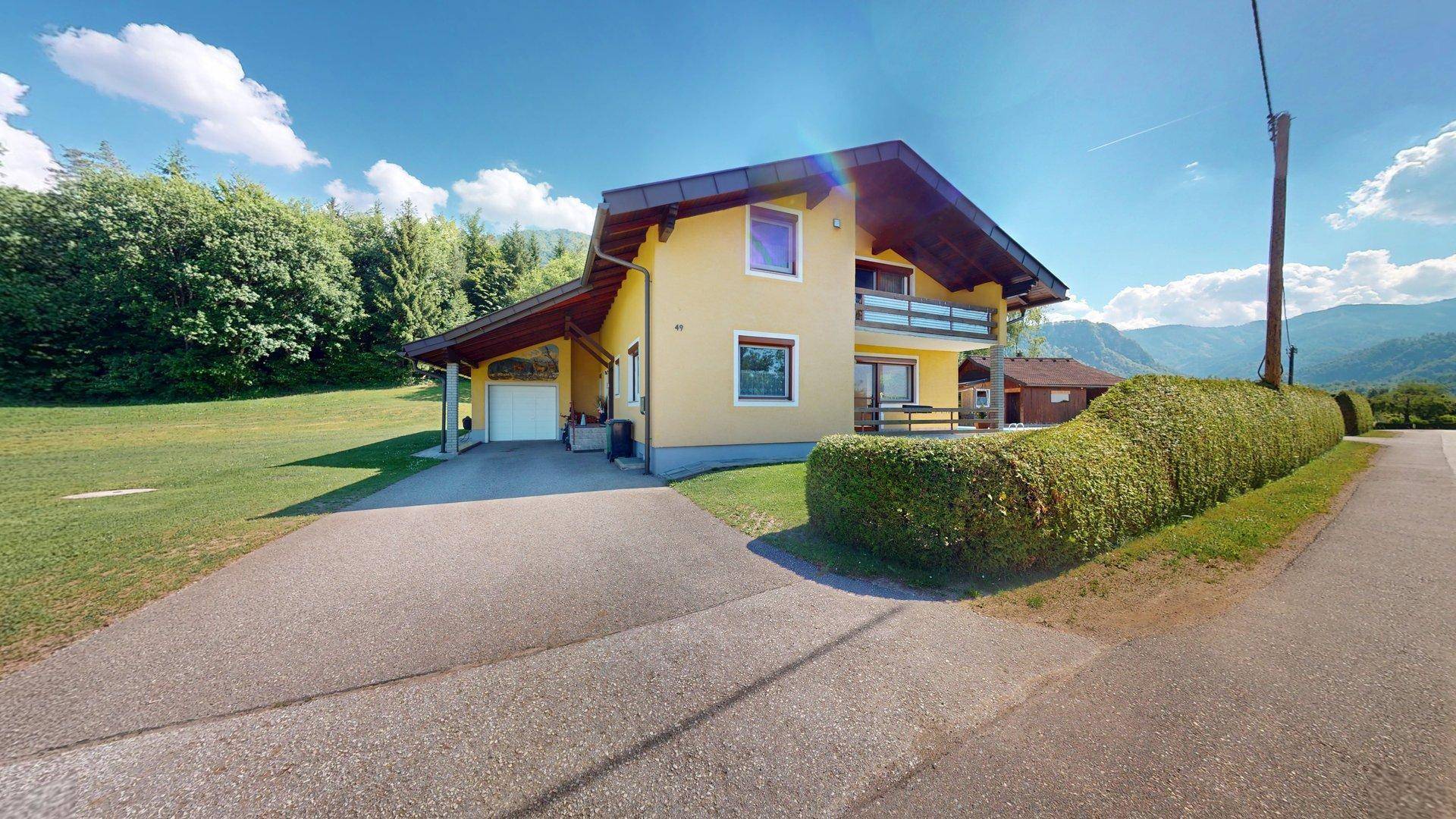 Das Haupthaus mit Carport und Zufahrt, umgeben von grünen Hecken und Bäumen.