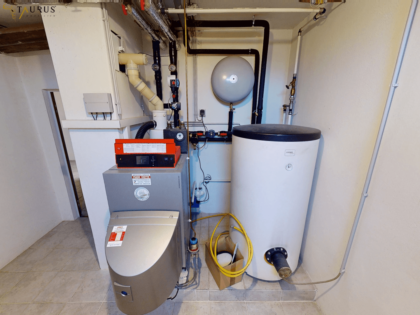 Heizungsraum im Keller mit Warmwasserspeicher und technischen Installationen.