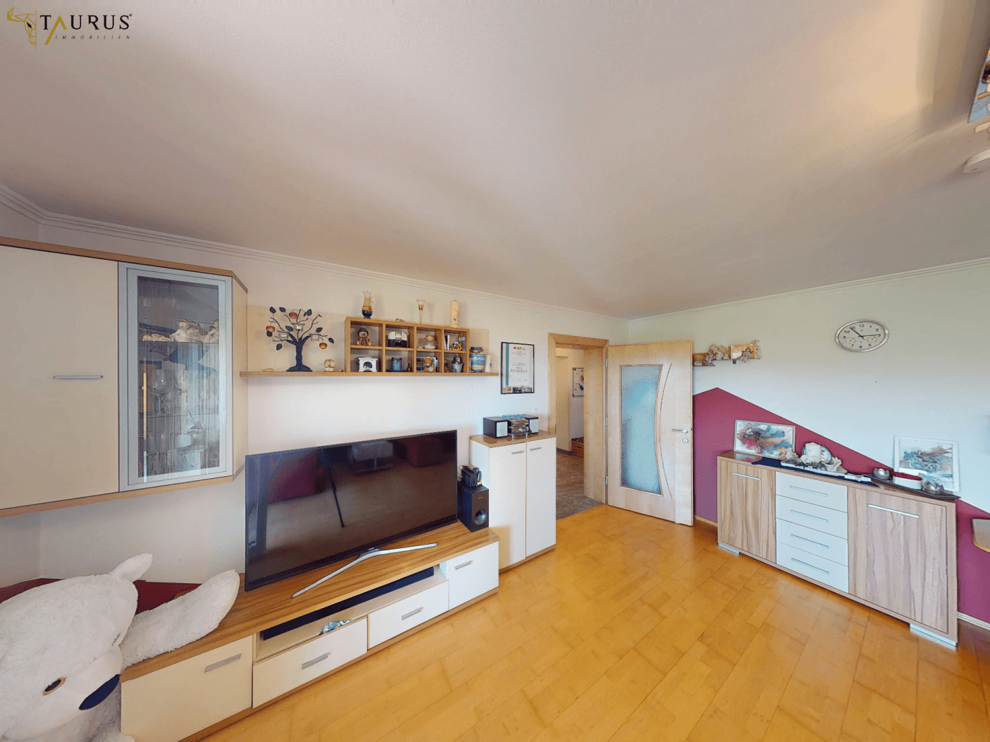 Geräumiges Wohnzimmer mit großem Fernseher, modernen Schränken und Holzfußboden.
