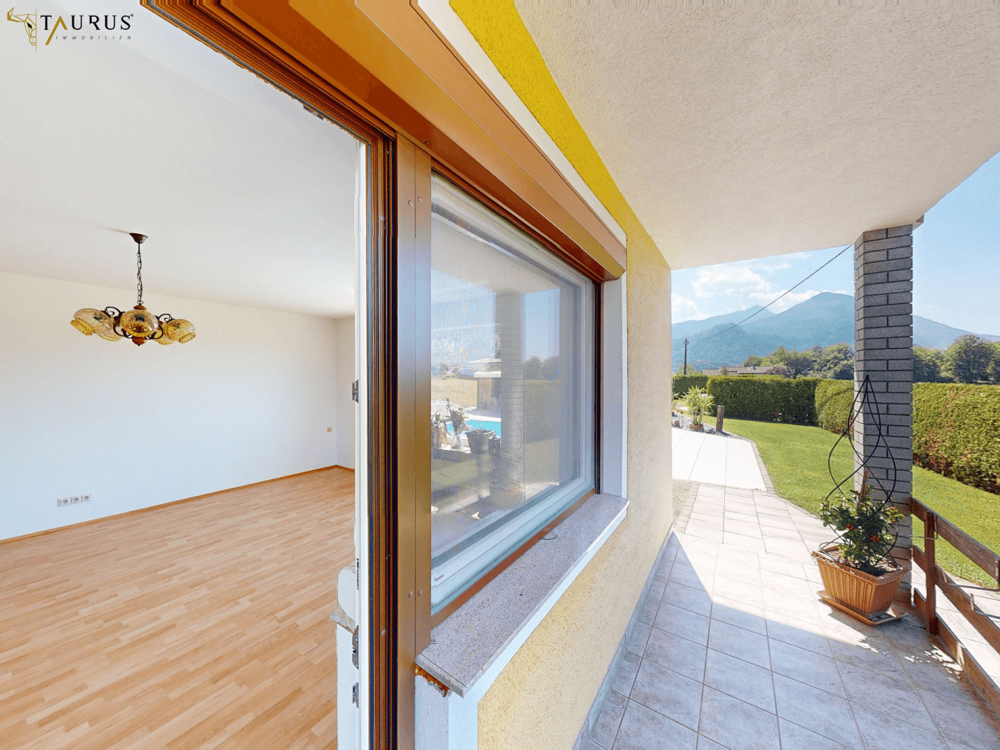 Blick von der Terrasse in das helle Wohnzimmer mit Parkettboden und Bergblick.