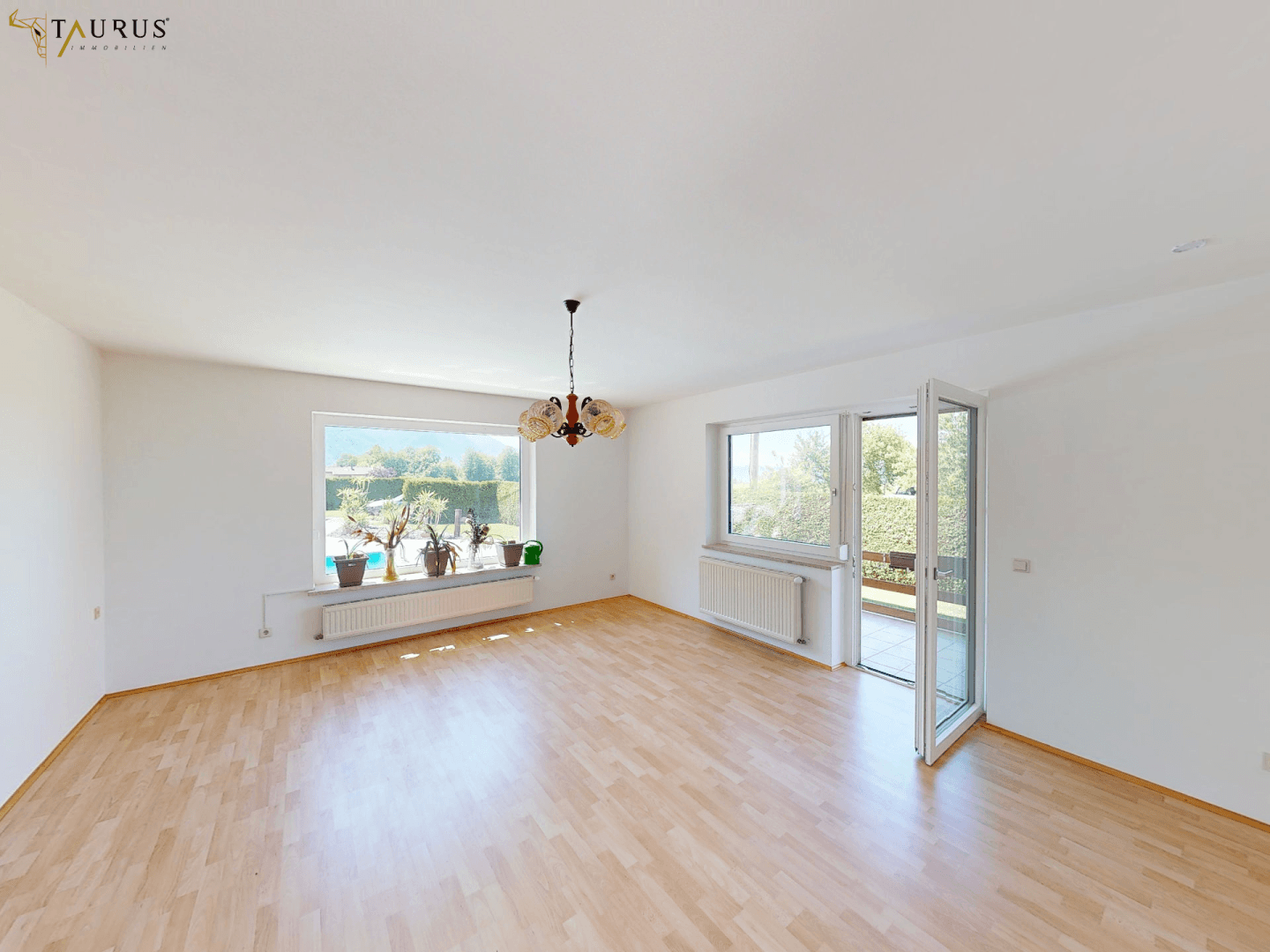 Geräumiges Wohnzimmer mit Parkettboden, großen Fenstern und Zugang zur Terrasse.