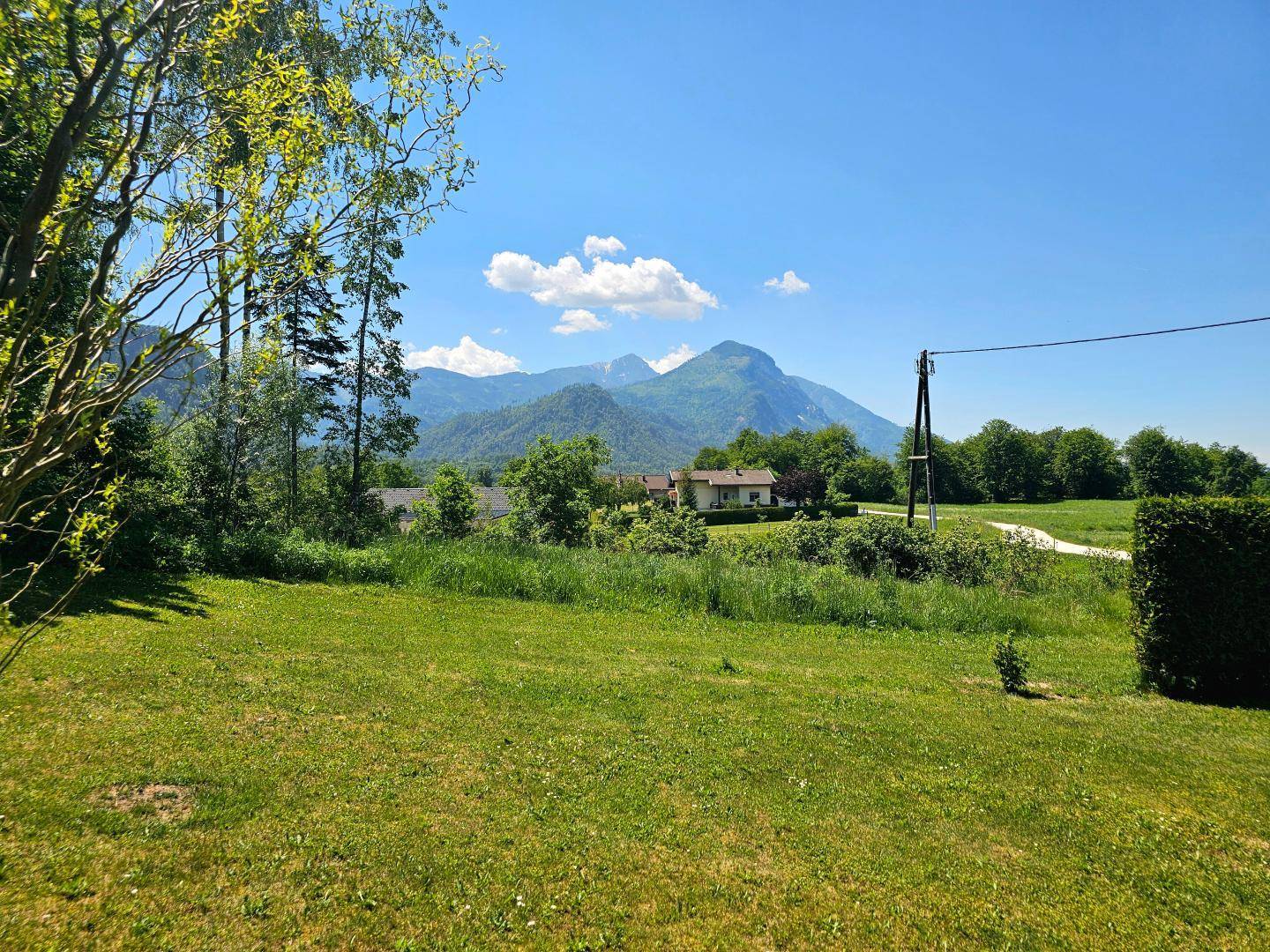 Weitläufiger Blick auf die umliegende Berglandschaft und grüne Wiesen unter blauem Himmel.