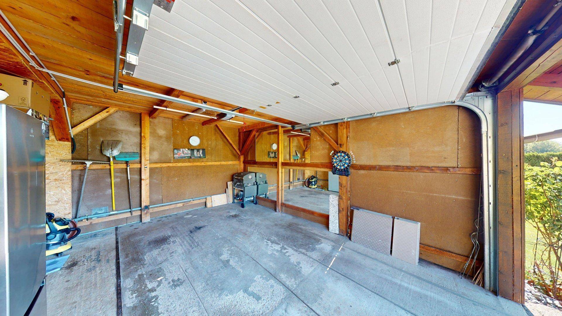 Geräumige Garage mit Holzbalken und Stauraum, ideal für Fahrzeuge und Werkzeuge.