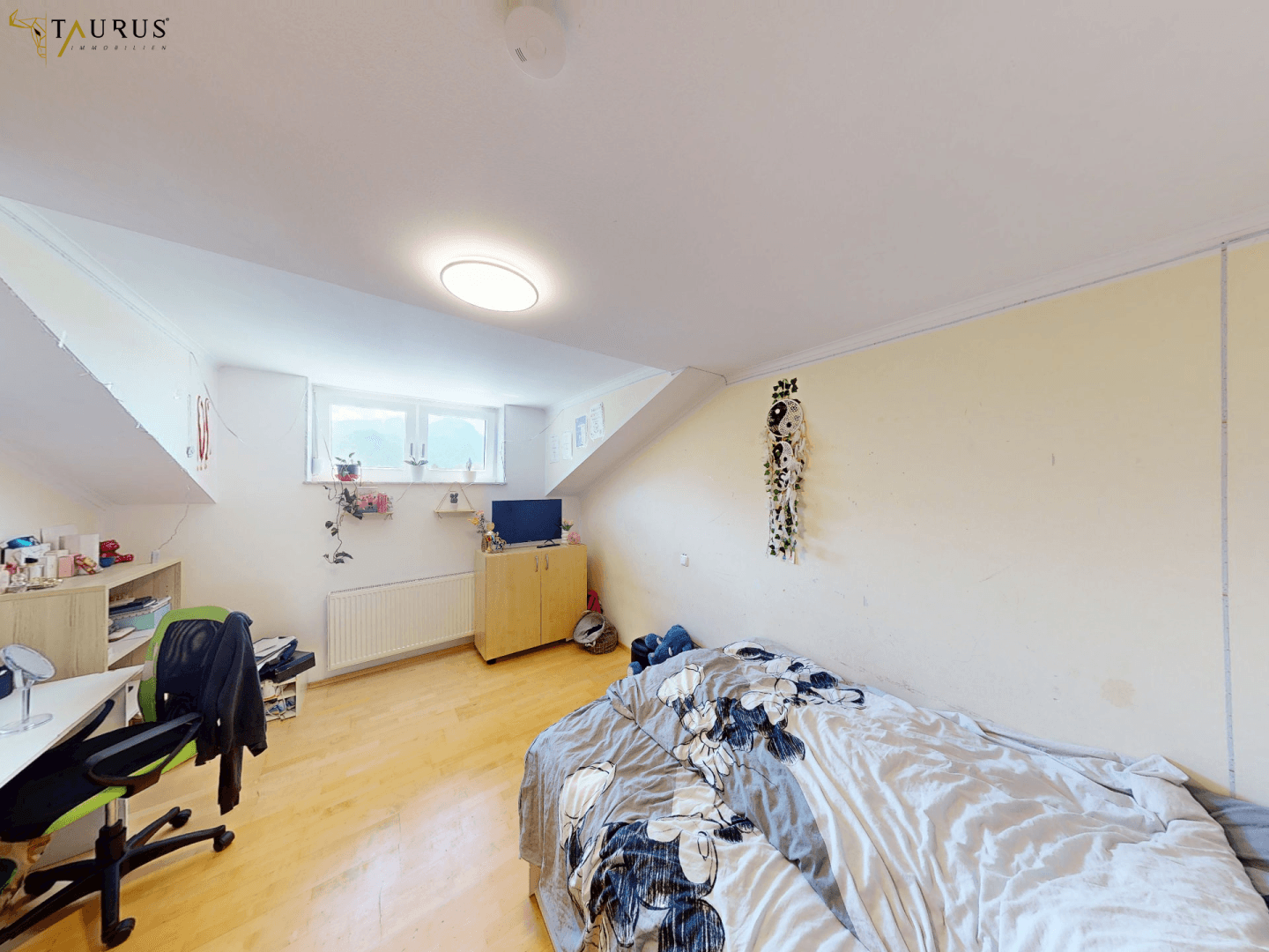 Gemütliches Schlafzimmer mit Bett, Schreibtisch und Fenster unter einer Dachschräge.