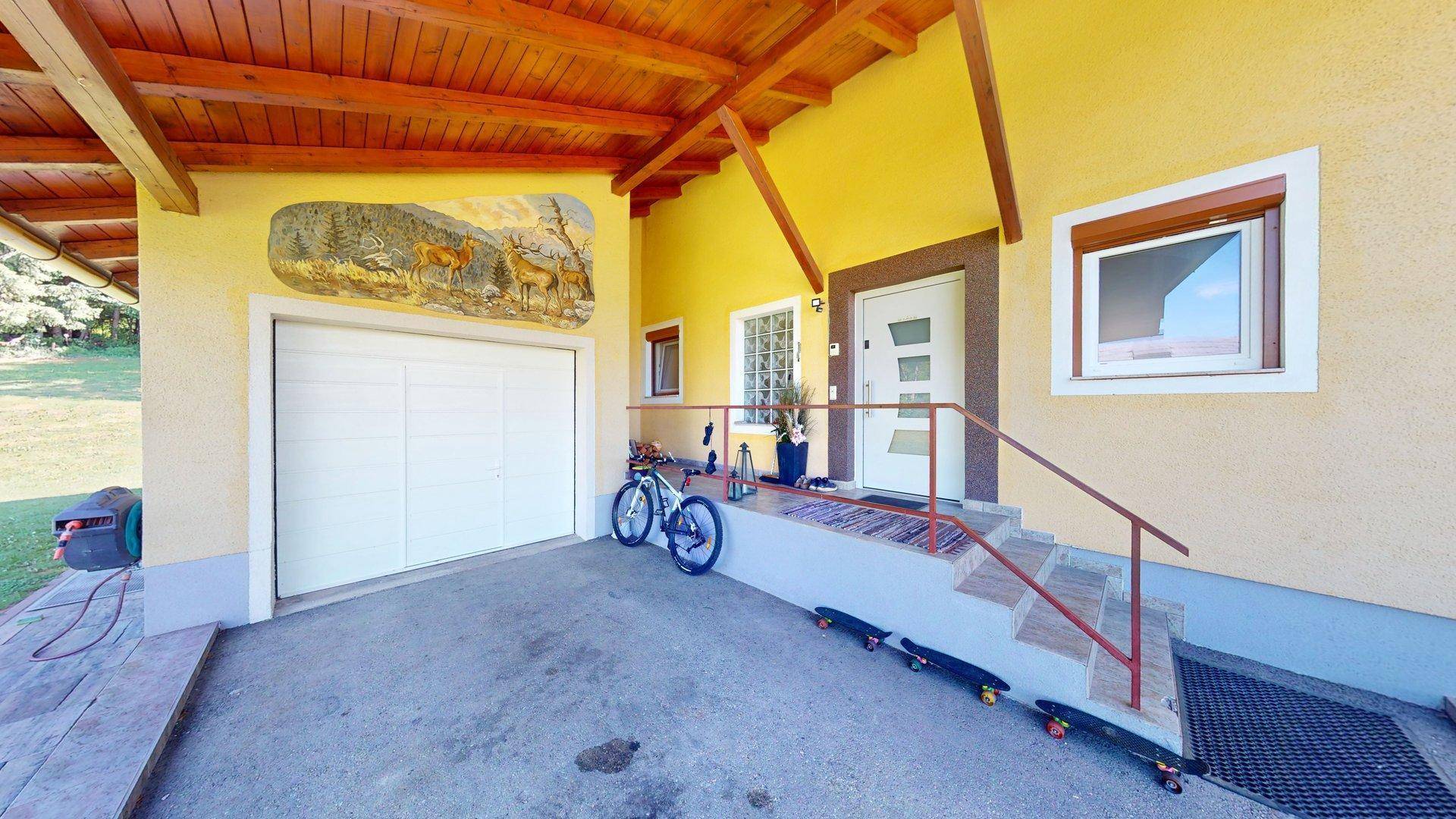 Überdachter Eingangsbereich mit Carport und Zugang zur Garage, geschmückt mit einem Wandgemälde.