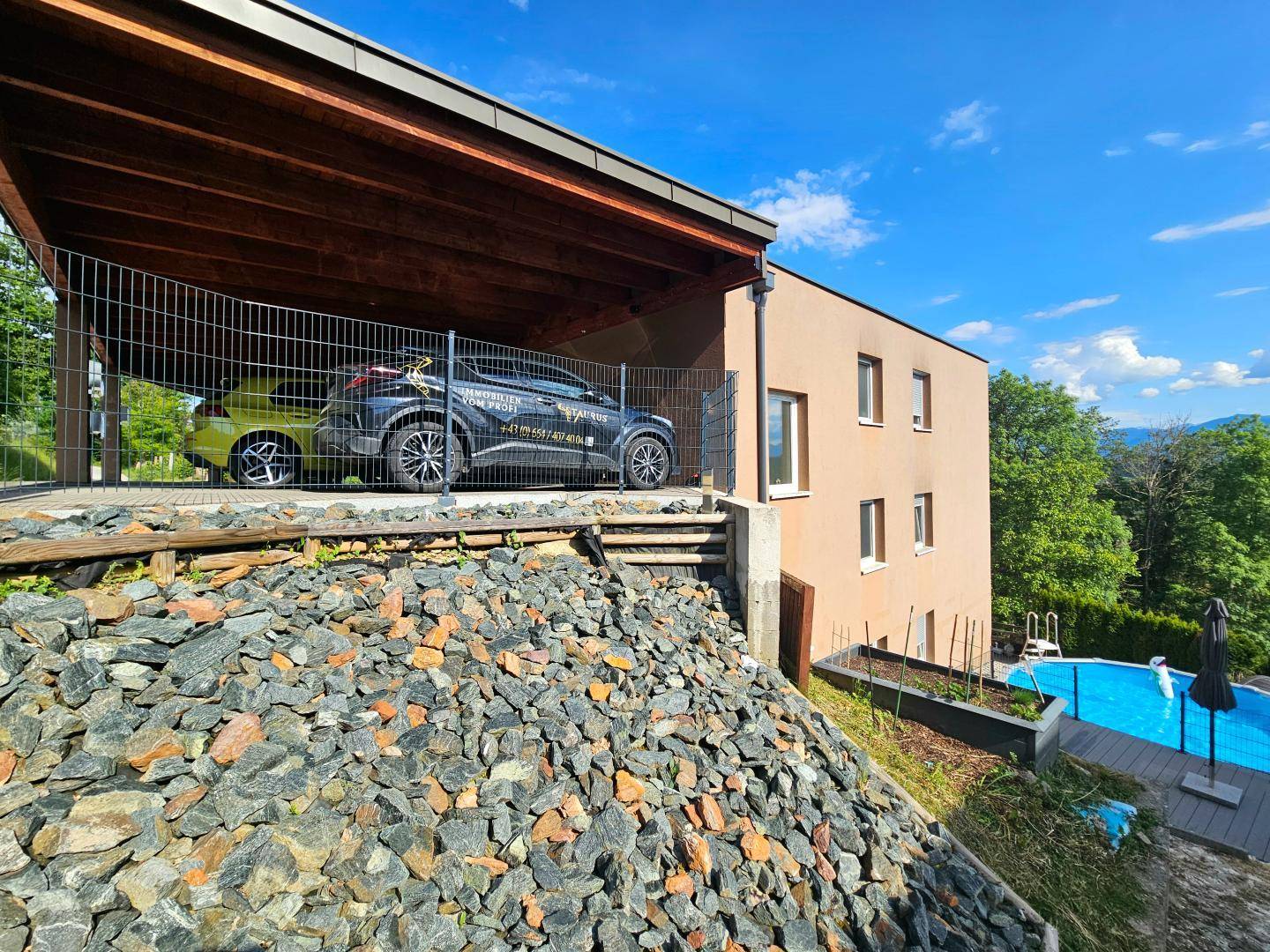 Seitenansicht des modernen Hauses mit Carport, Steinschüttung und Poolbereich.