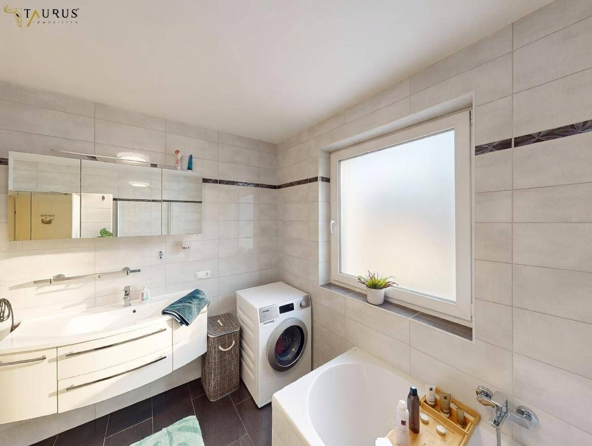 Helles Badezimmer mit Waschbecken, Spiegelschrank, Badewanne und Fenster.