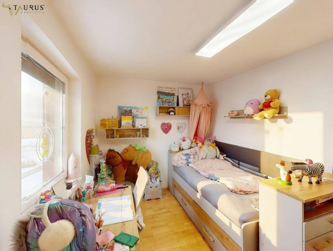 Freundliches Kinderzimmer mit Holzboden, Schreibtisch und Spielzeug.