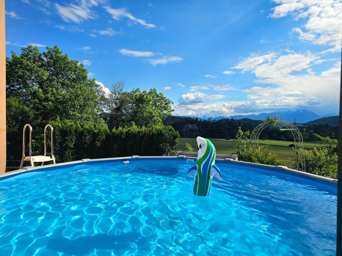 Aufstellpool mit aufblasbarem Spielzeug und weitem Blick auf die Berge und grüne Landschaft.