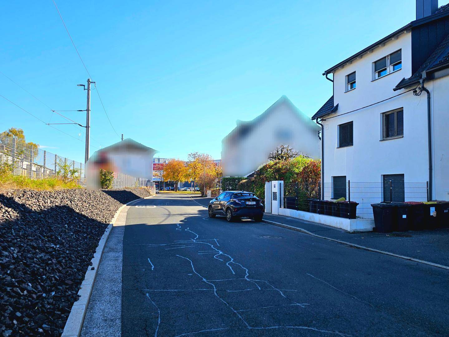 Wohnhaus an einer ruhigen Straße mit parkendem Auto und herbstlicher Vegetation.
