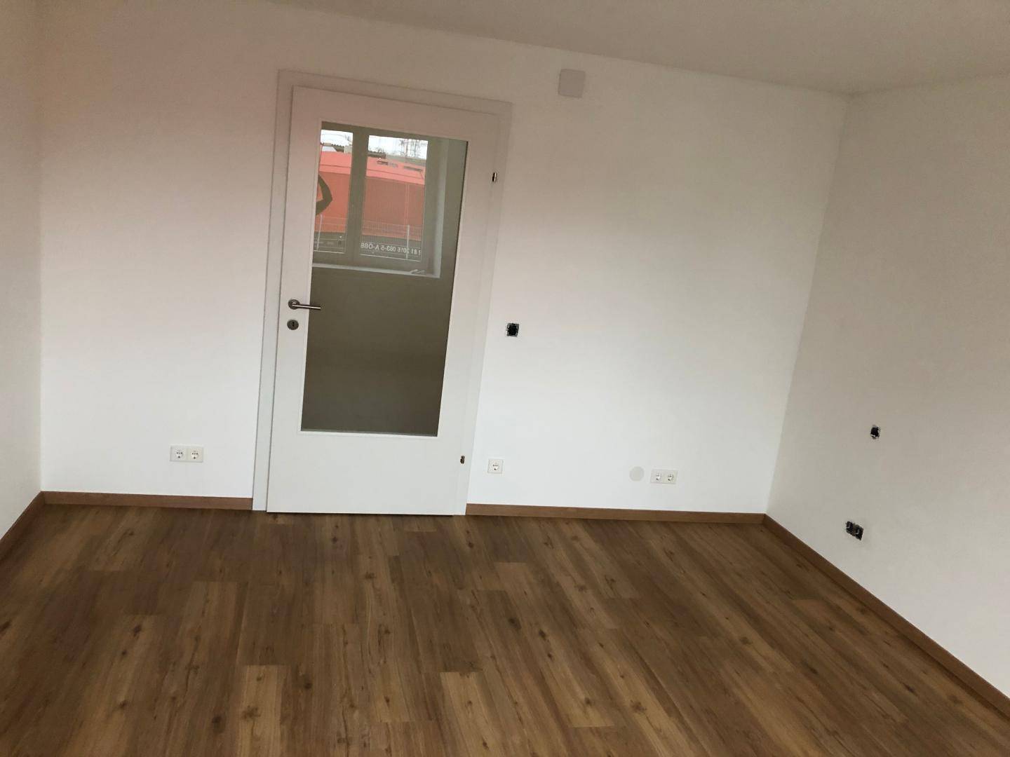 Helles Zimmer mit Laminatboden und einer Tür mit Glaseinsatz.
