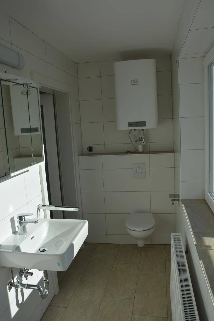 Helles Badezimmer mit WC, Waschbecken, Spiegelschrank und Fenster.