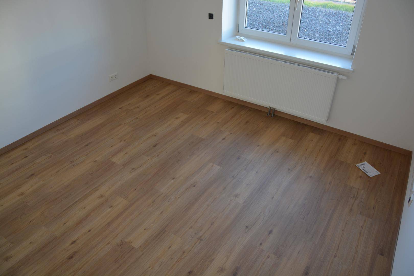 Leeres Zimmer mit neuem Laminatboden und einem Fenster mit Heizkörper.